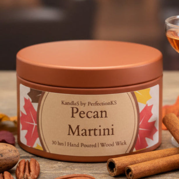 A round metal candle tin labeled 'Pecan Martini' by KandleS by PerfectionKS, sitting on a dark wooden surface with a softly blurred background.