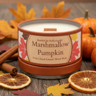 A candle tin labeled 'Marshmallow Pumpkin' by Kandles by PerfectionKS, with a terracotta-colored lid and base, white wax, and fall leaf graphics on the label, set on a dark wooden surface.