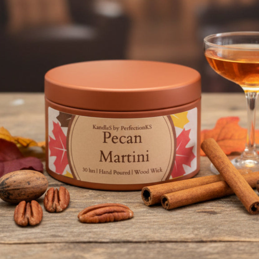 A round metal candle tin labeled 'Pecan Martini' by KandleS by PerfectionKS, sitting on a dark wooden surface with a softly blurred background.